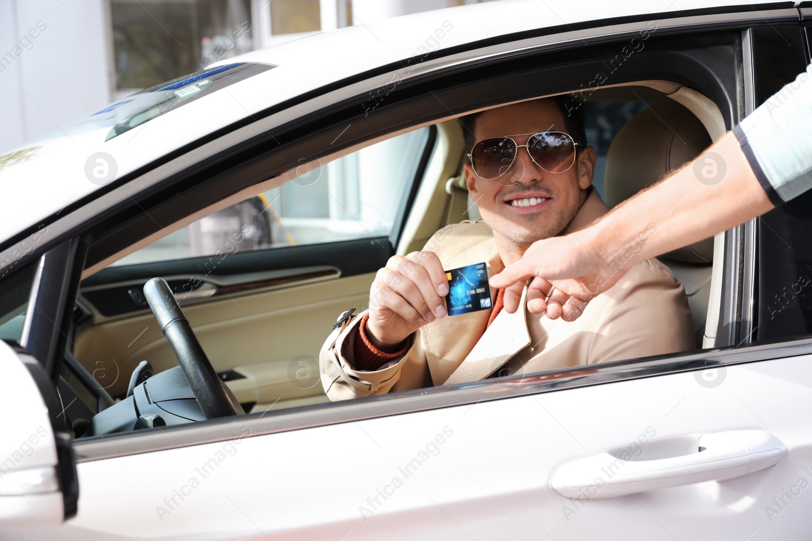 Photo of Man sitting in car and giving credit card to worker at gas station