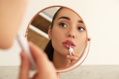 Woman with herpes applying cream onto lip in front of mirror 