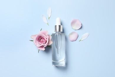 Photo of Bottle of cosmetic serum, beautiful flower and petals on light blue background, flat lay