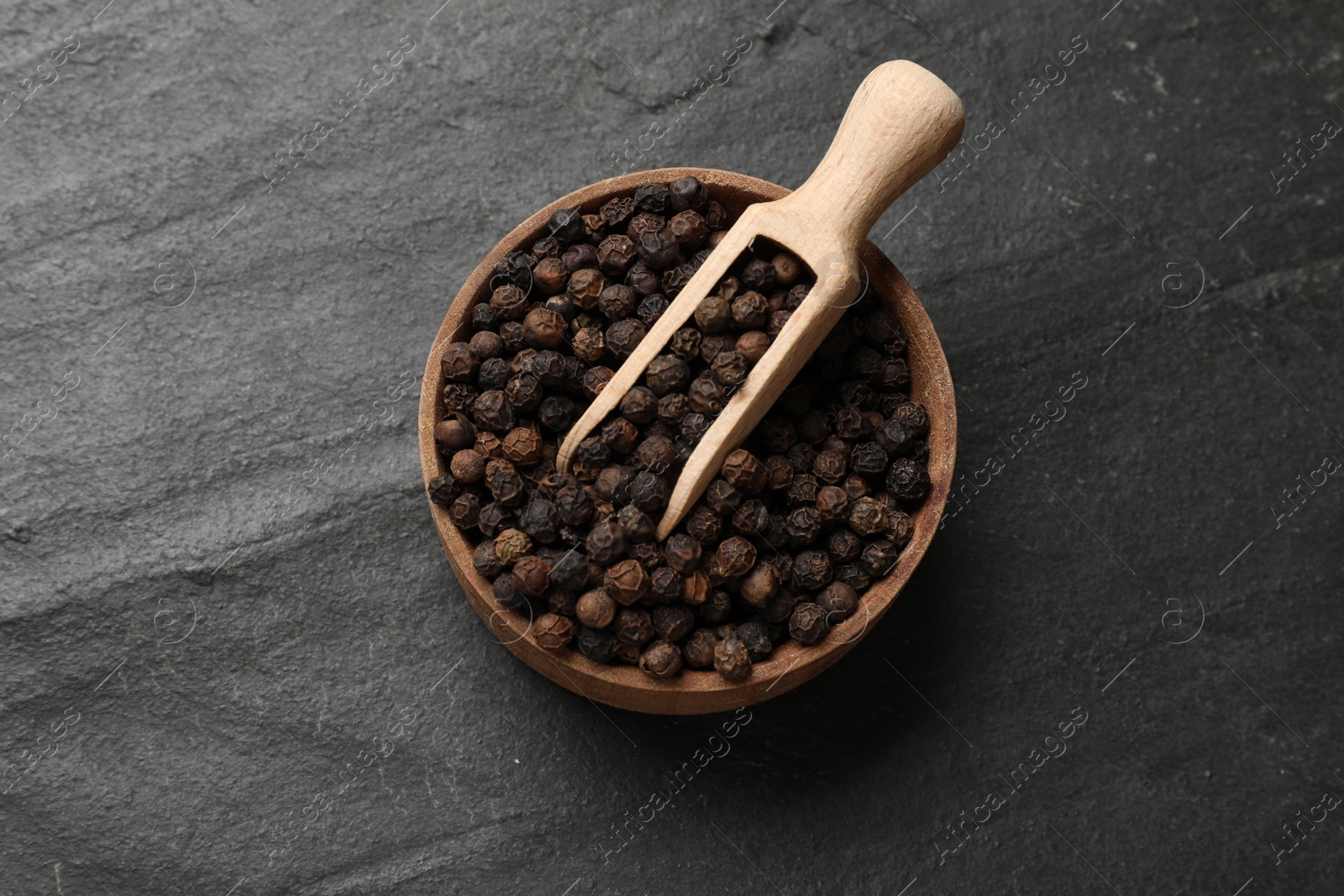 Photo of Aromatic spice. Pepper in bowl and scoop on black table, top view