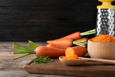 Photo of Board with fresh and grated carrots on wooden table