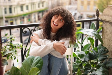 Beautiful young woman relaxing in chair surrounded by green houseplants on balcony