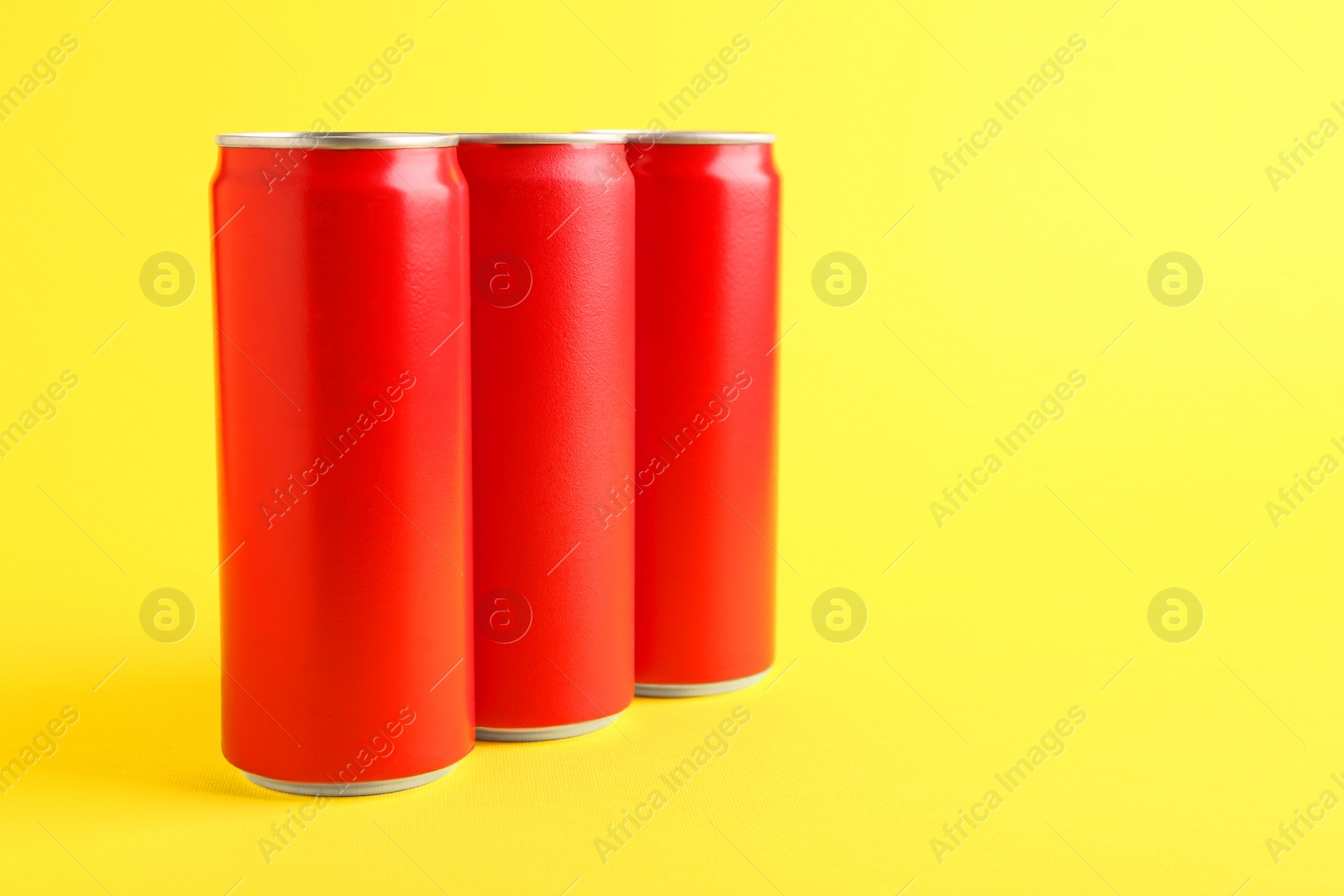 Photo of Energy drinks in red cans on yellow background, space for text