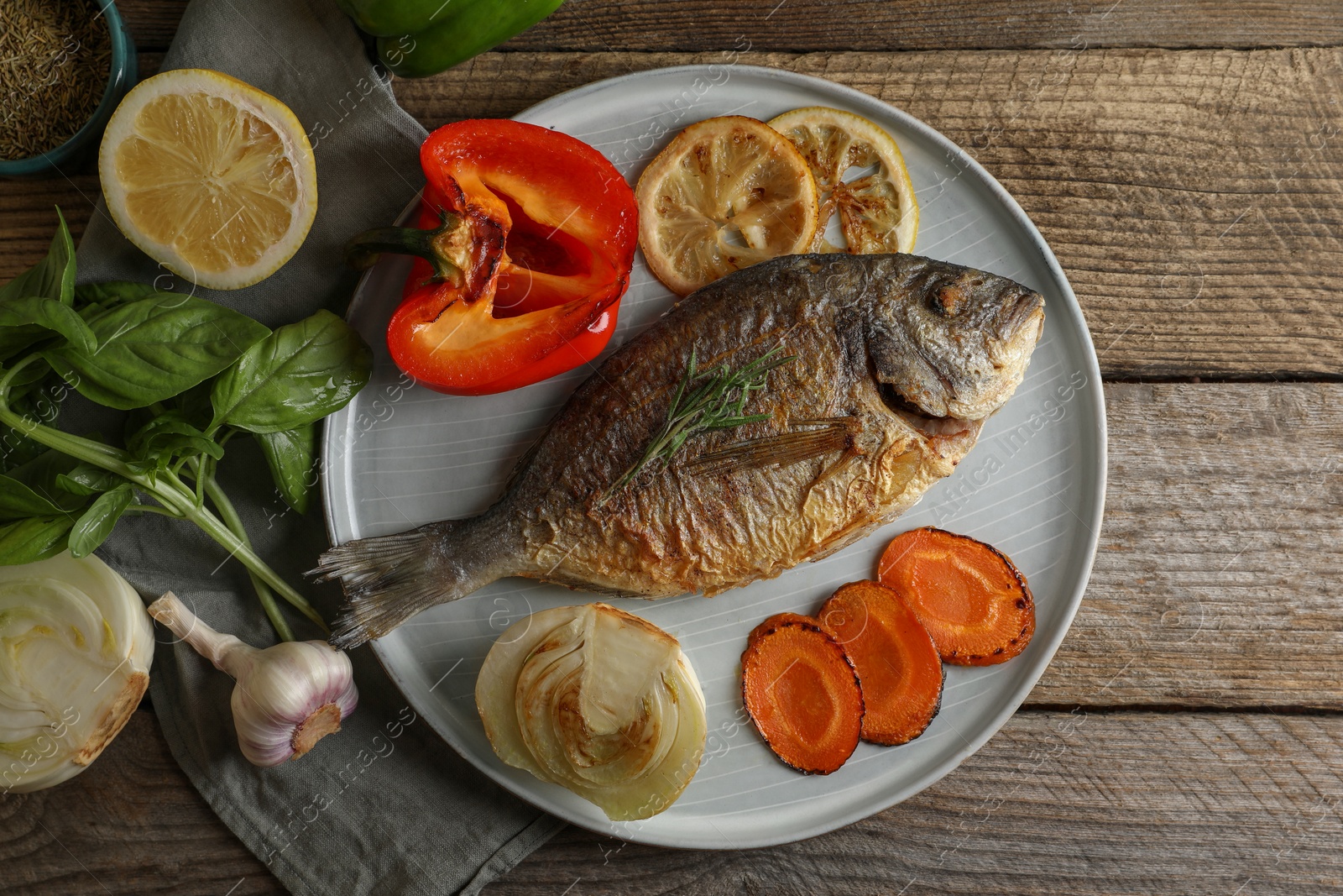 Photo of Delicious dorado fish with vegetables and herbs served on wooden table, flat lay