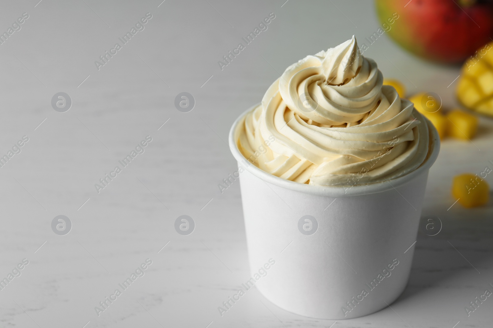 Photo of Cup with tasty frozen yogurt on light wooden table. Space for text