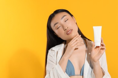 Photo of Beautiful young woman holding sun protection cream on orange background, space for text