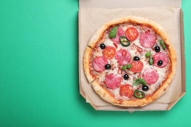 Photo of Delicious pizza Diablo in cardboard box on green background, top view. Space for text