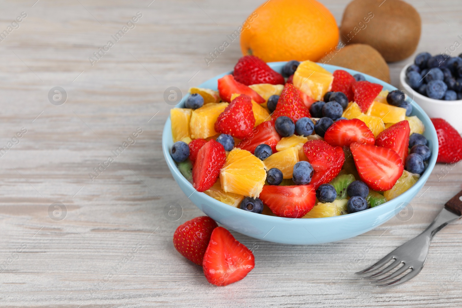 Photo of Delicious fresh fruit salad in bowl served on wooden table. Space for text