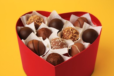 Photo of Heart shaped box with delicious chocolate candies on yellow background, closeup