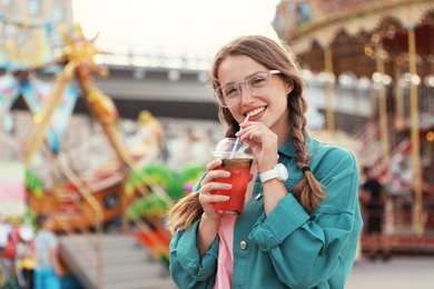 Photo of Young woman with refreshing drink in amusement park. Space for text