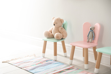 Photo of Cute toys on chairs with bunny ears near white wall indoors. Children's room interior