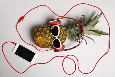 Pineapple with headphones and smartphone on grey background, top view