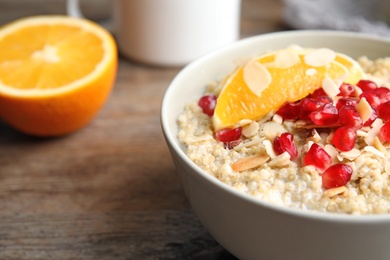 Photo of Bowl of quinoa porridge with nuts, orange and pomegranate seeds on wooden table, closeup
