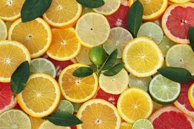 Photo of Different citrus fruits and green leaves as background, top view