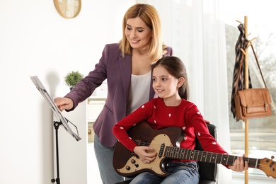 Photo of Little girl playing guitar with her teacher at music lesson. Learning notes