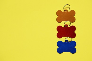 Color metal pet tags on yellow background, flat lay. Space for text