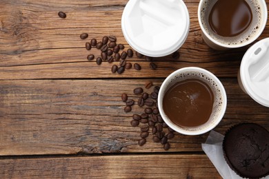 Coffee to go. Paper cups with tasty drink, muffin and beans on wooden table, flat lay. Space for text