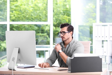 Handsome young man working with computer at table in office