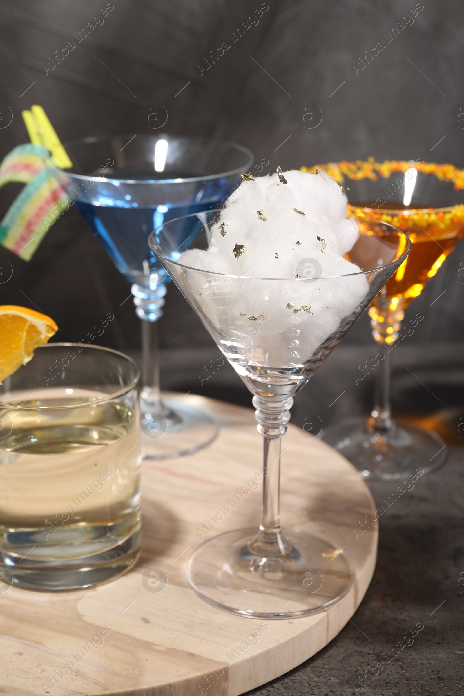 Photo of Tasty cotton candy cocktail and other alcoholic drinks in glasses on gray textured table