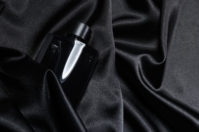 Photo of Luxury men's perfume in bottle on black satin fabric, top view. Space for text