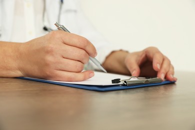 Doctor writing at wooden table, closeup view