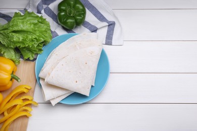 Photo of Delicious folded Armenian lavash and fresh vegetables on white wooden table, flat lay. Space for text