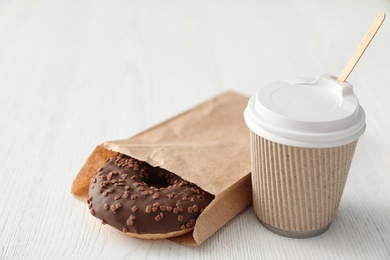 Tasty donut in paper bag and coffee on wooden table. Space for text
