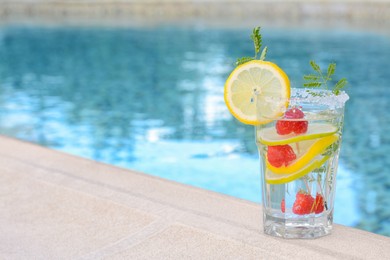 Photo of Delicious refreshing lemonade with raspberries near swimming pool, space for text