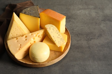 Photo of Wooden plate with different sorts of cheese on grey table, space for text