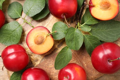 Photo of Delicious ripe cherry plums with leaves on wooden table, flat lay