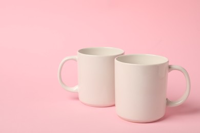 Photo of Two white ceramic mugs on pink background, space for text