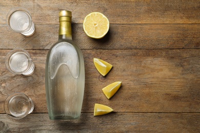 Photo of Bottle of vodka, lemon and shot glasses on wooden table, flat lay. Space for text