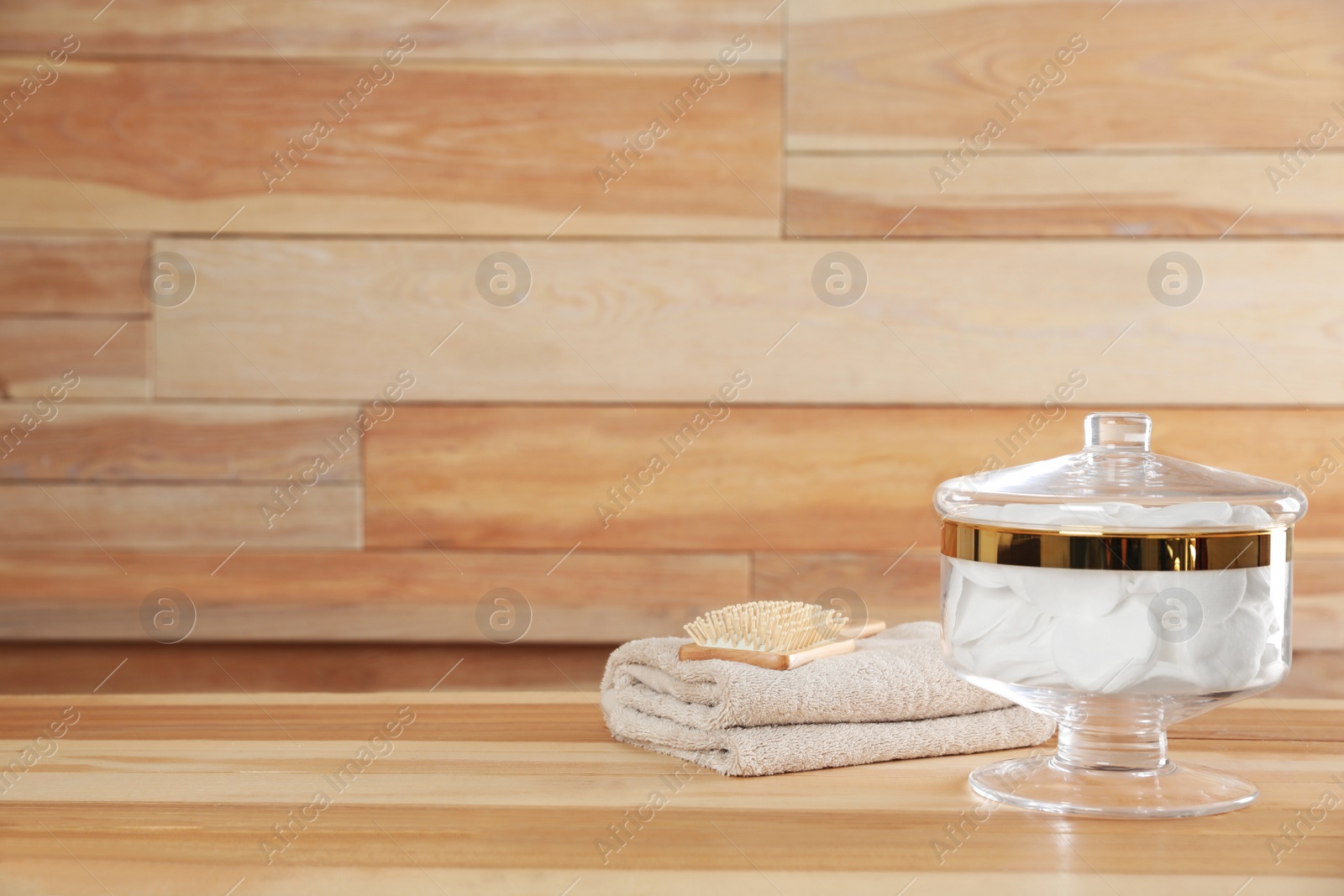 Photo of Decorative glass jar with cotton pads, towel and hairbrush on table against wooden background. Space for text