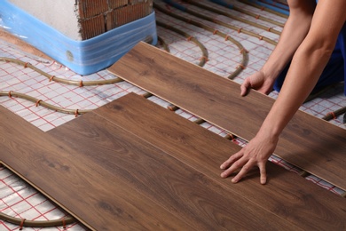 Photo of Worker installing new wooden laminate over underfloor heating system, closeup