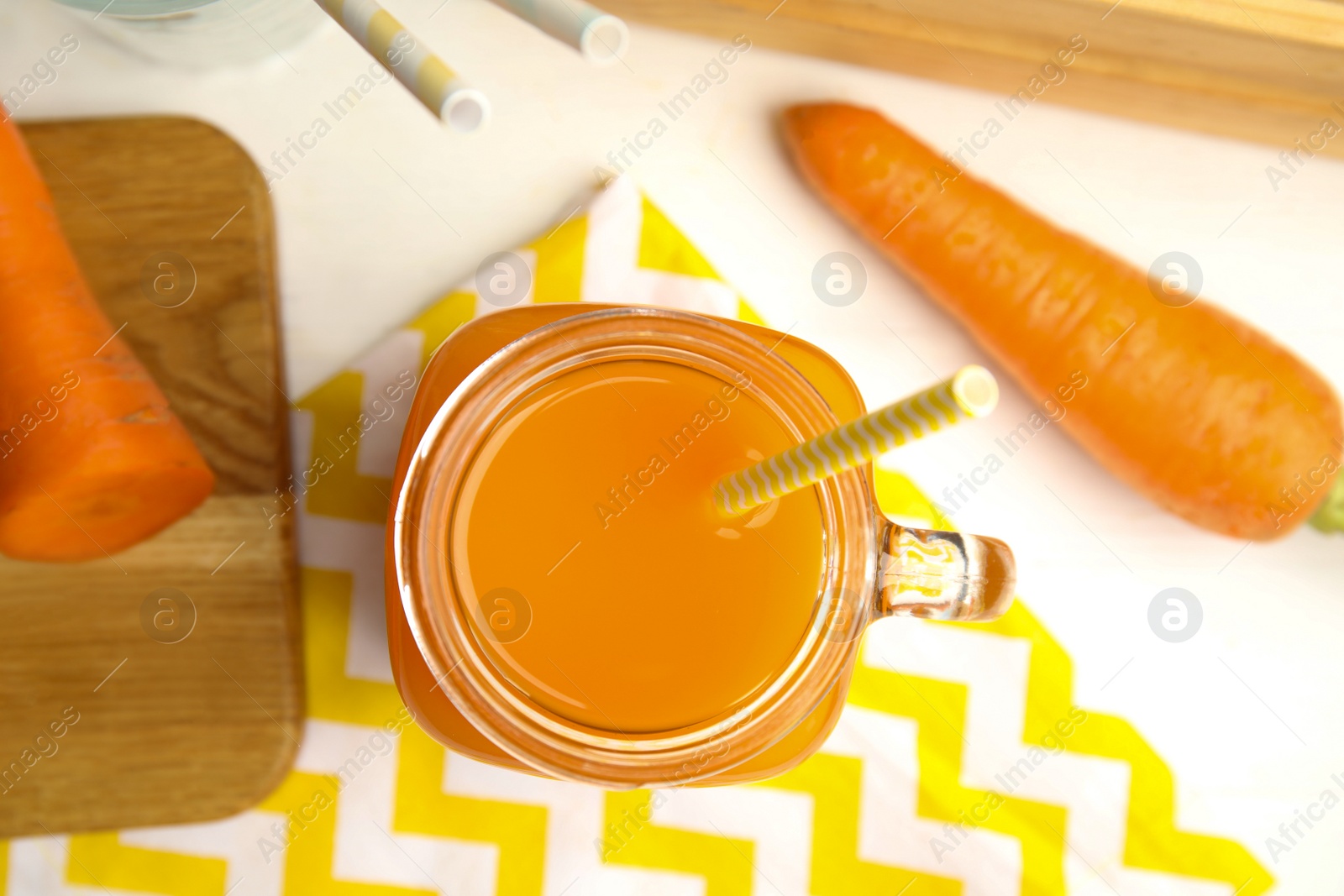 Photo of Freshly made carrot juice in mason jar on white table, flat lay