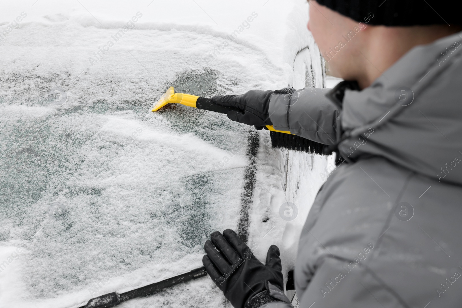 Photo of Man cleaning snow from car windshield outdoors, closeup