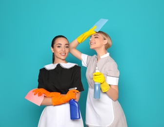 Young chambermaids with rags and detergents on color background