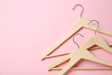 Wooden hangers on pink background, top view. Space for text