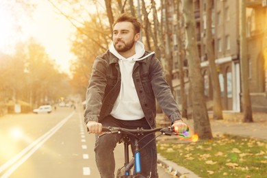 Image of Happy handsome man riding bicycle in city on sunny day
