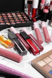 Bright lip glosses among different cosmetic products on white dressing table