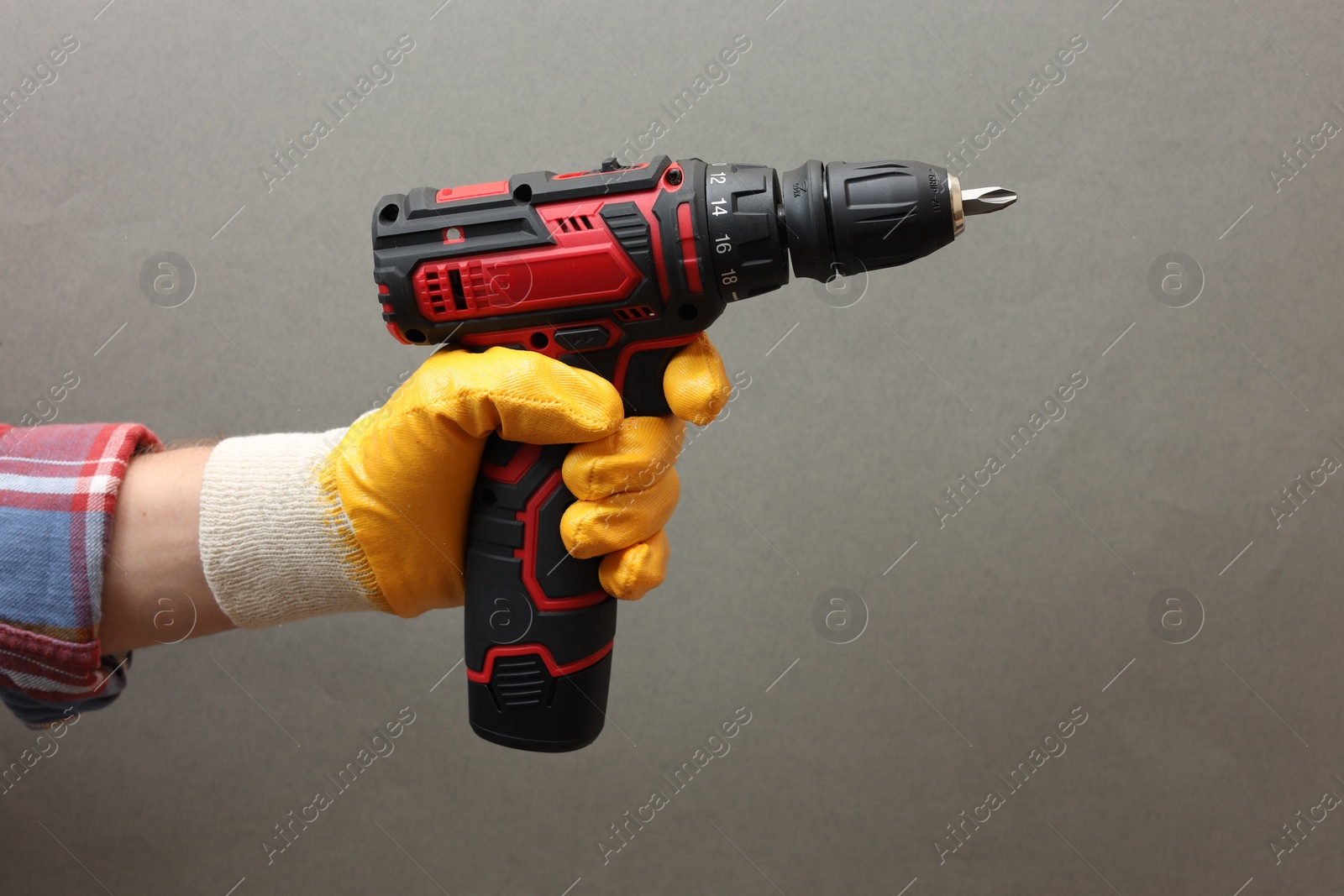 Photo of Handyman holding electric screwdriver on grey background, closeup