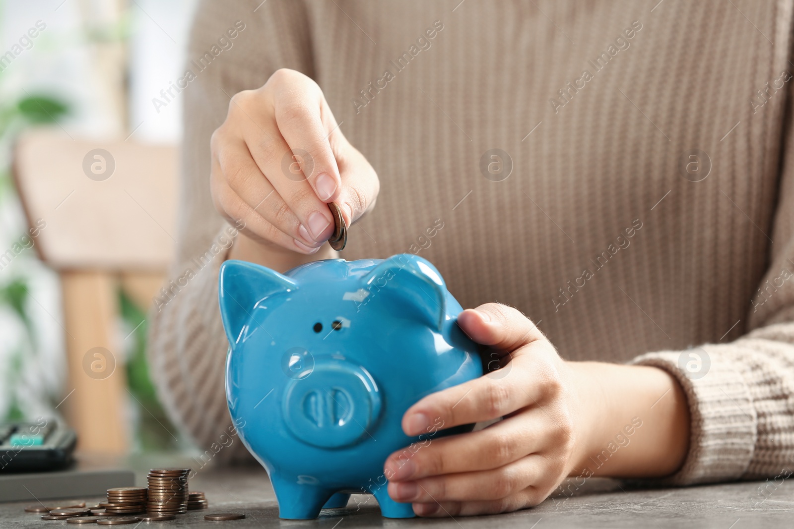 Photo of Woman putting money into piggy bank at table, closeup