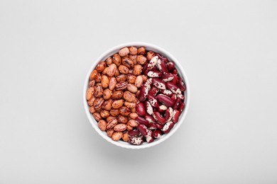 Photo of Different kinds of kidney beans in bowl on white background, top view