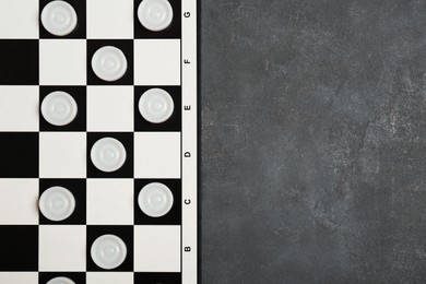 Photo of Checkerboard with game pieces on grey table, top view. Space for text