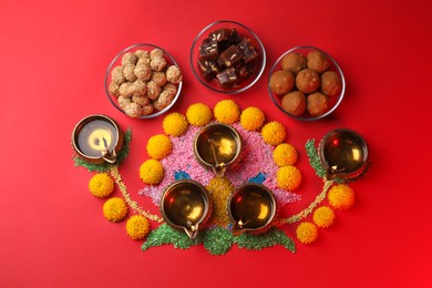 Photo of Happy Diwali. Flat lay composition with diya lamps, colorful rangoli and Indian sweets on red table