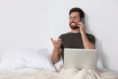 Photo of Handsome man talking on phone while working with laptop in bed, space for text