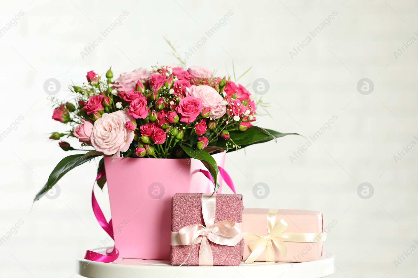 Photo of Beautiful bouquet of flowers and gift boxes on table against light background. Space for text