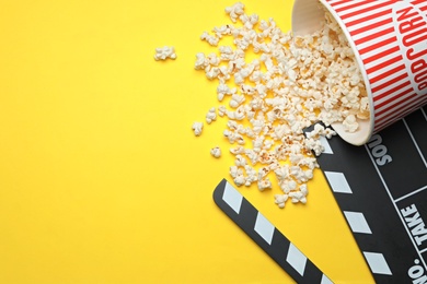 Photo of Clapperboard and popcorn on yellow background, flat lay with space for text. Cinema snack