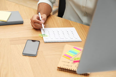 Photo of Man making schedule using calendar at table in office, closeup