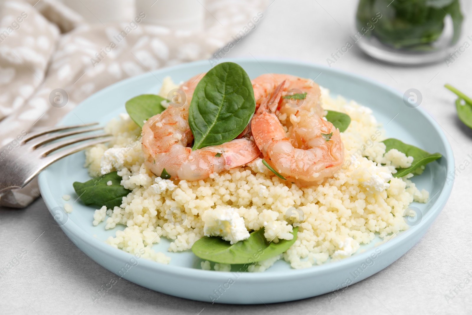 Photo of Delicious couscous with shrimps and spinach served on white table, closeup